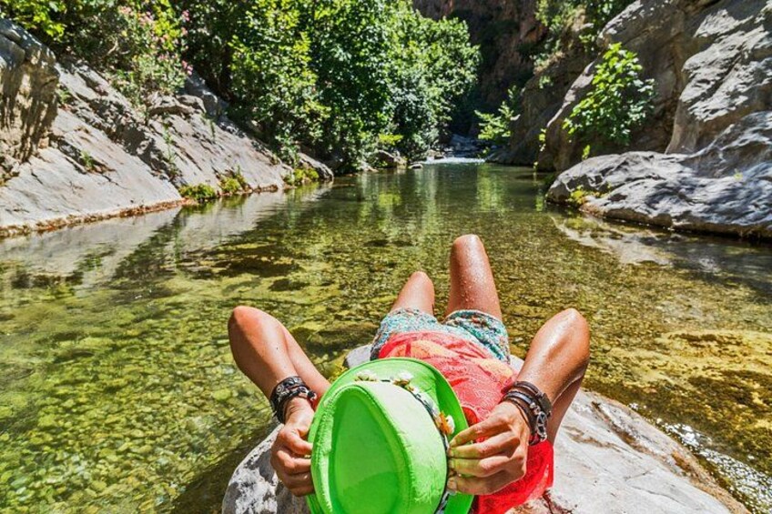 A person relaxing on a rock by a clear river surrounded by greenery. 2