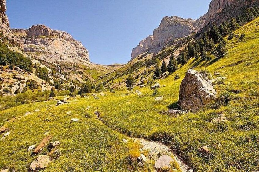 Een bergachtig landschap met een grasachtig dal, rotsformaties en een heldere lucht. 4