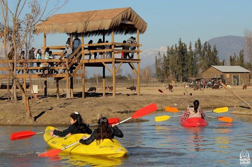 People kayaking on a river, a wooden structure with people on it, and a building in the background. 2