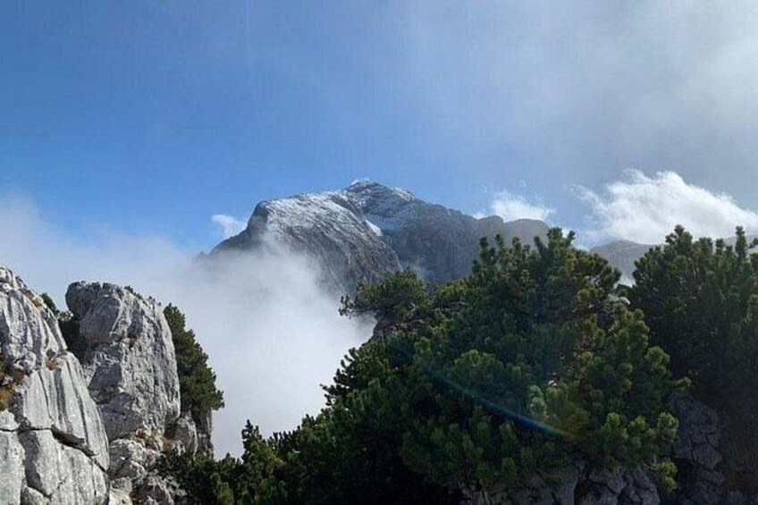 A mountain with a snow-capped peak, surrounded by clouds and rocky terrain. 5