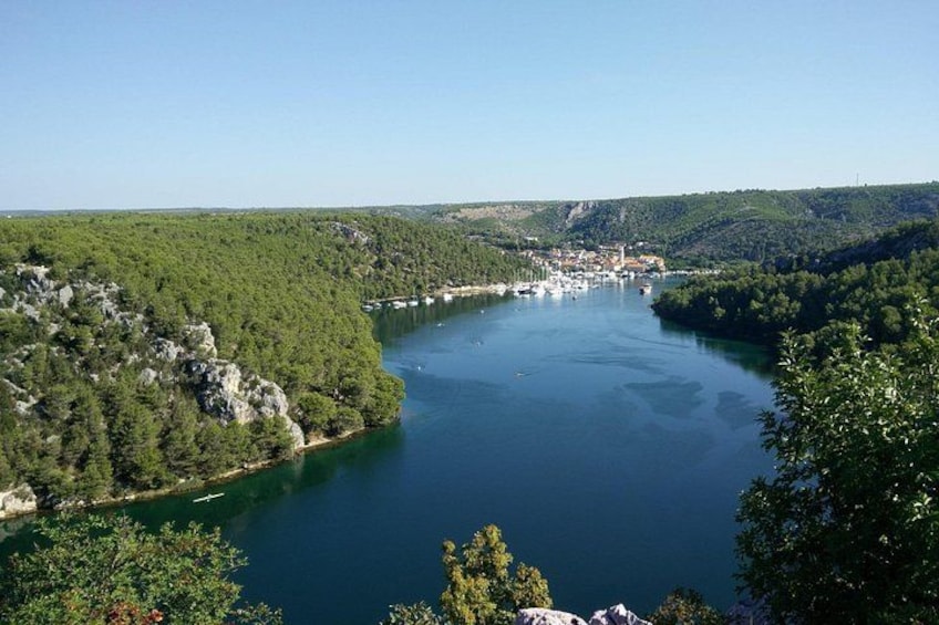 A lake surrounded by forested hills, a small town, and boats on the water. 4