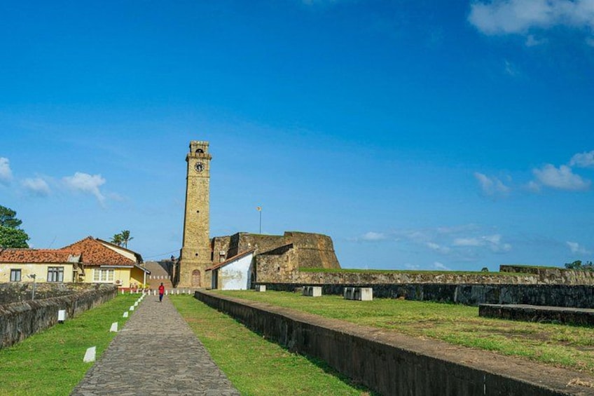 A historical fort with a tall tower, a paved pathway, and surrounding grassy areas. 2