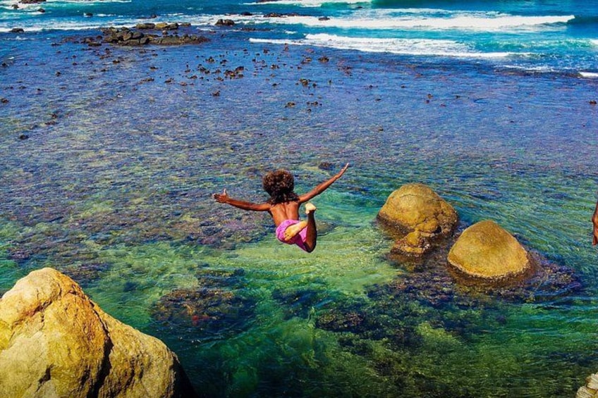 A person diving into clear blue water near rocks. 3