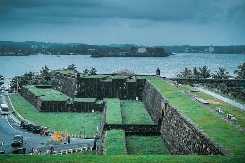 A large fort with green grass, a road, and a body of water in the background. 1
