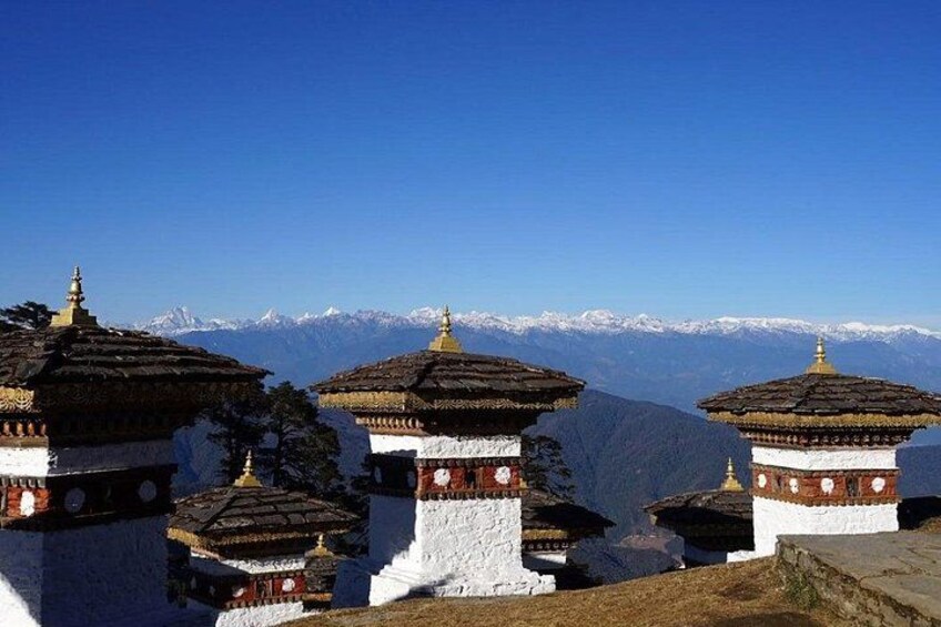 A row of traditional Tibetan prayer wheels with snow-capped mountains in the background. 3