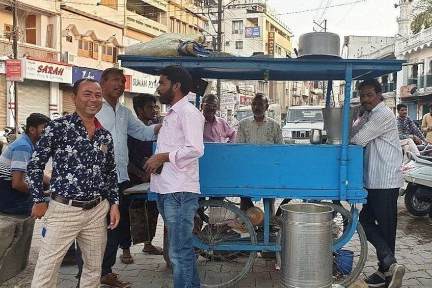 A blue cart with a metal container, a man in a pink shirt, and another man in a floral shirt standing nearby. 2