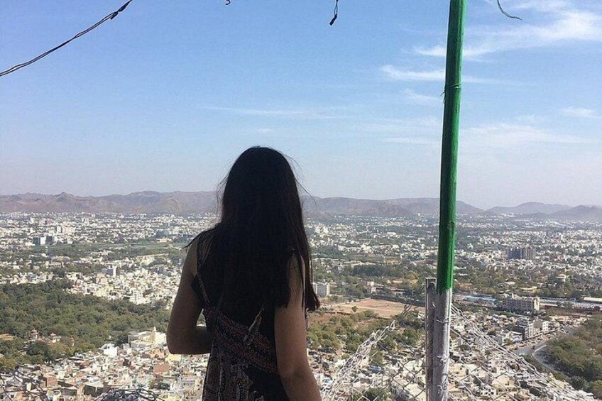 A person standing on a balcony overlooking a cityscape with buildings and hills in the distance. 4