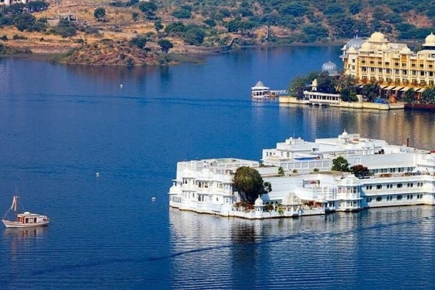 A large white building with multiple levels on a lake, surrounded by water and a few boats. 1