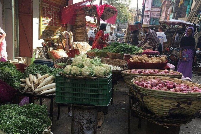 A bustling street market with various vegetables like cauliflower and potatoes displayed in baskets and crates. 3