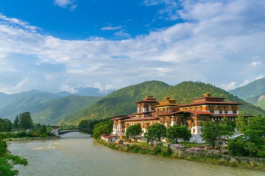 A traditional building by a river with mountains in the background. 2