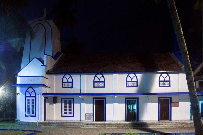 A white building with blue trim and arched windows, a bell tower, and a paved entrance. 3