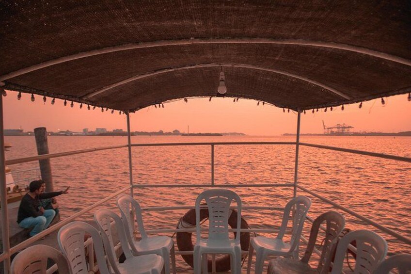 A boat with a covered deck, plastic chairs, and a person sitting on the edge. 5