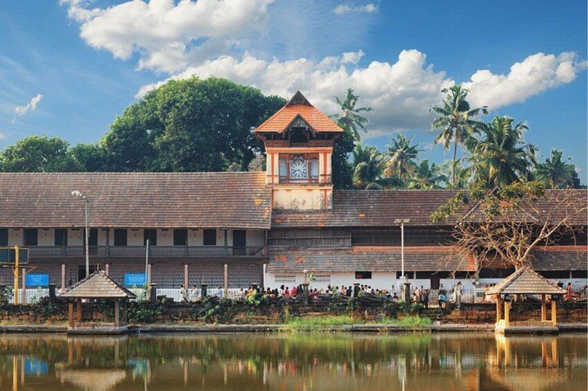 A building with a clock tower, palm trees, and a body of water reflecting the structure. 4