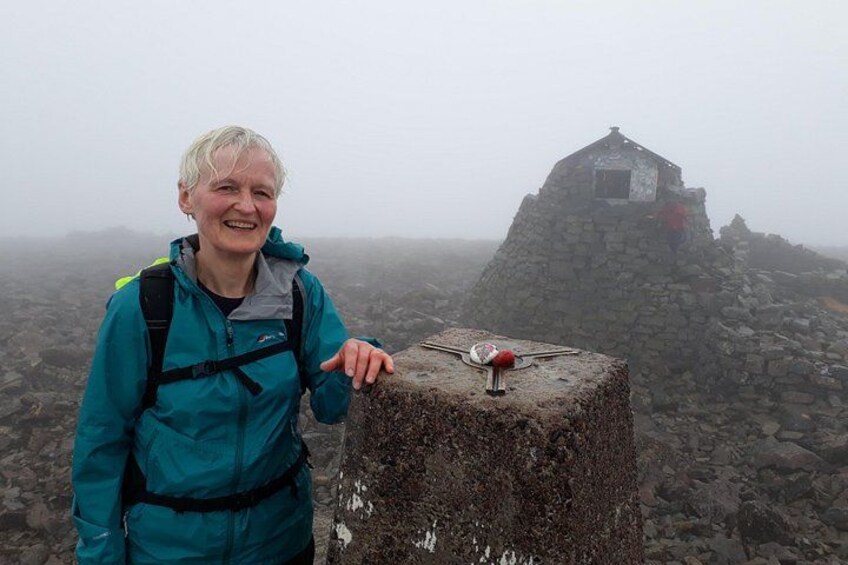 A person standing on a rocky outcrop with a small hut in the background. 1