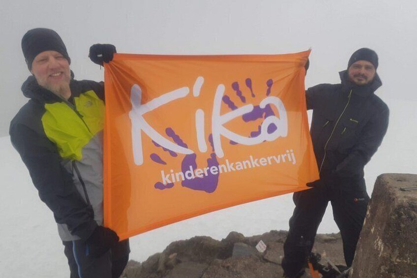 Two people holding an orange flag with white and purple text. 5
