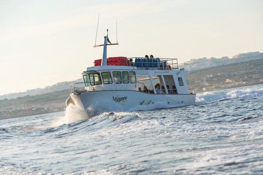 A white boat with the name 'Aphrodite' on its side, moving through choppy waters with a coastline in the background. 2