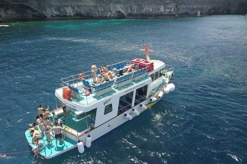 A boat with people on board, surrounded by clear blue water and rocky cliffs. 2
