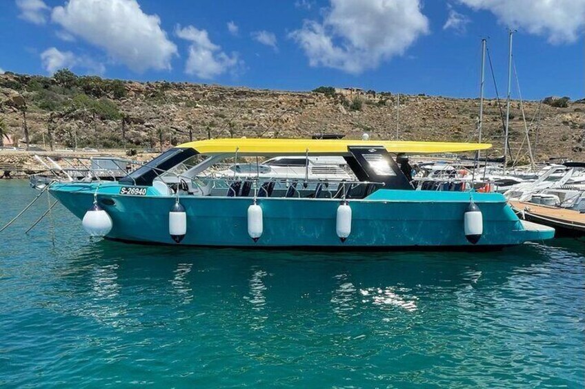 A turquoise boat with a yellow canopy docked at a marina with rocky hills in the background. 3