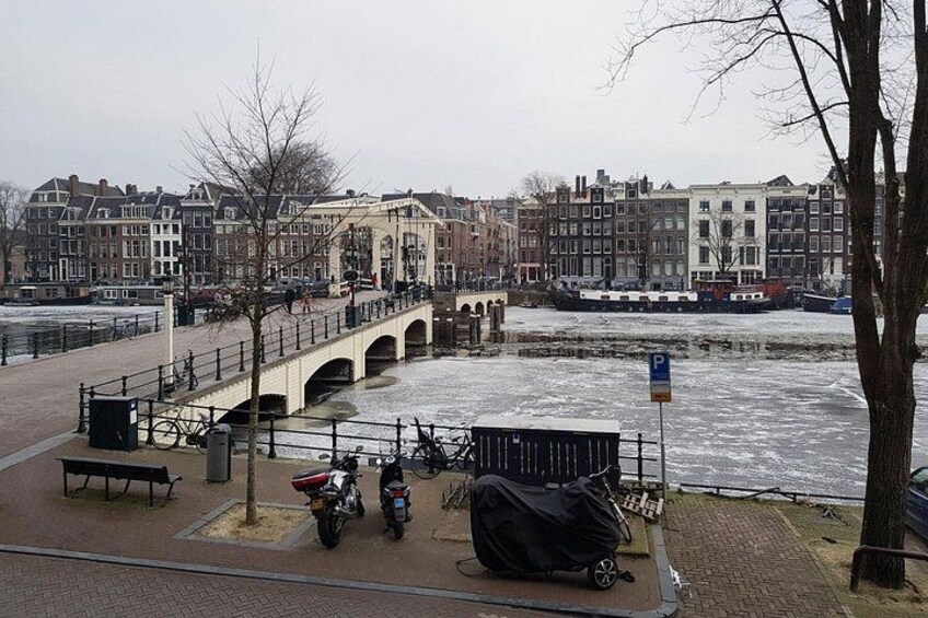 A canal with a bridge, parked bicycles, and a row of buildings in the background. 3
