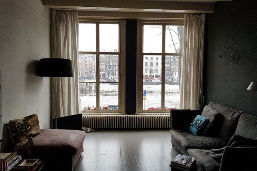 A living room with a large window, a brown sofa, a black lamp, and a radiator. 2