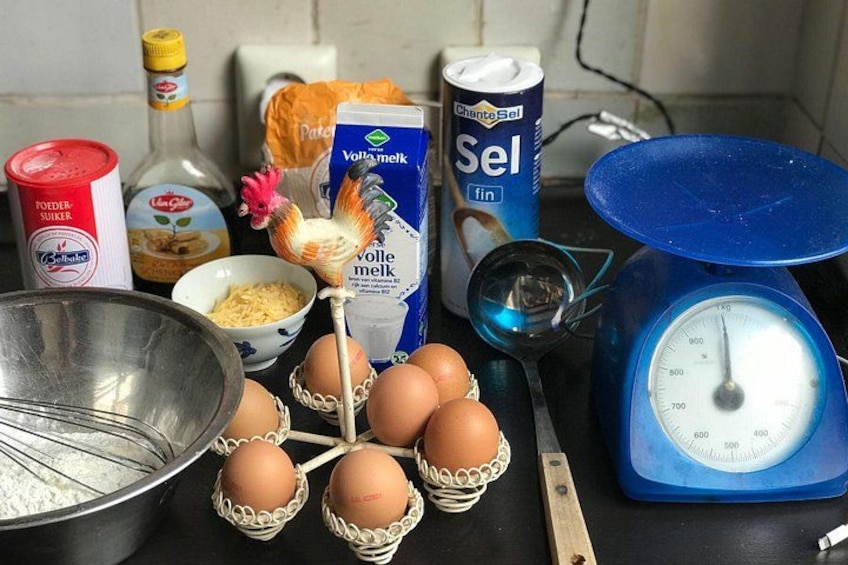 A kitchen counter with eggs, flour, a whisk, a measuring cup, and a scale. 4