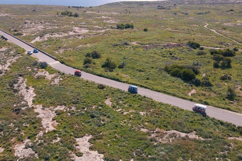 A road winding through a hilly landscape with sparse vegetation and a few vehicles traveling along it. 3