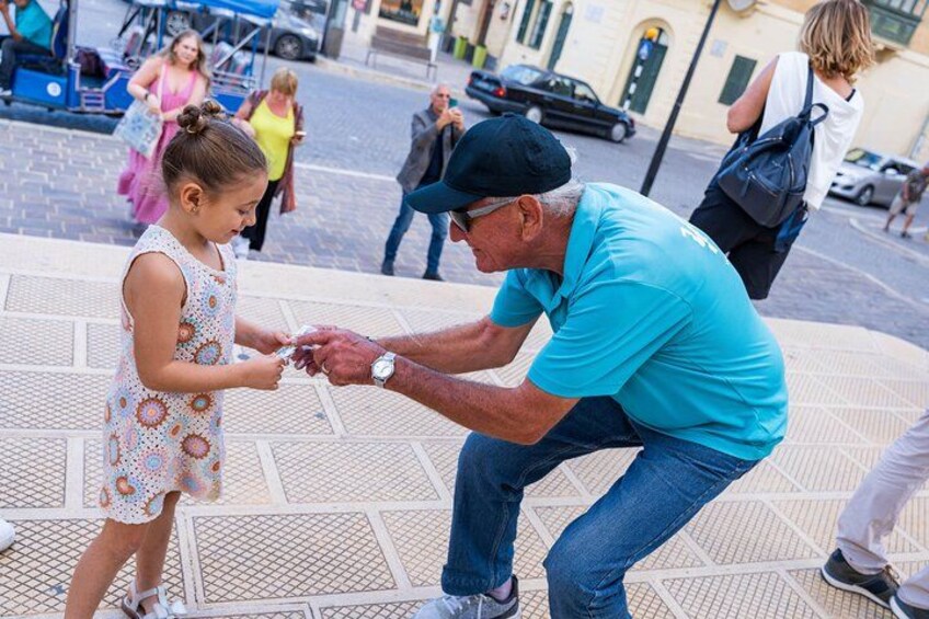 A man in a blue shirt and cap handing a coin to a young girl in a patterned dress. 2