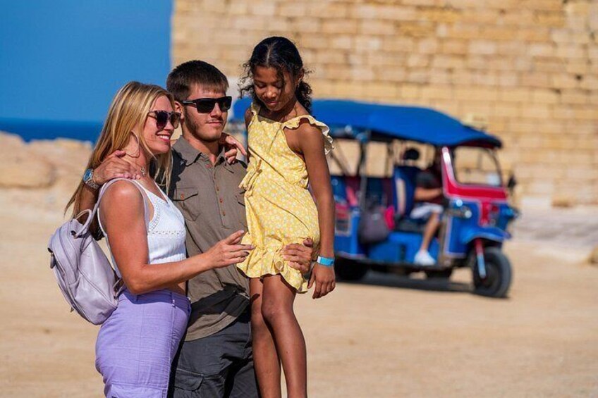 Eine Familie mit drei Personen neben einer historischen Steinmauer, im Hintergrund ein Tuk-Tuk. 5