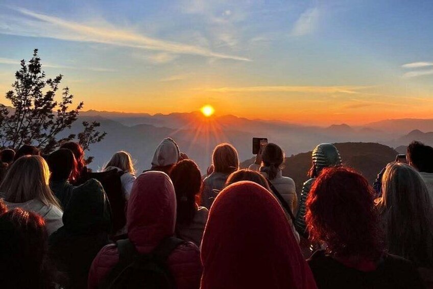 En gruppe mennesker betragter solnedgangen over et bjergrigt landskab. 1