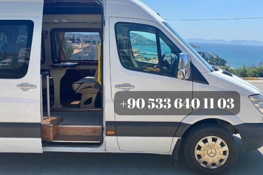 A white van with a phone number on the side, parked on a road with a scenic view of the sea and hills in the background. 1