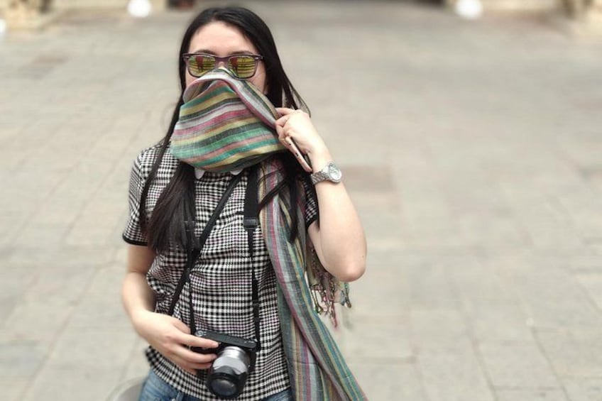 Een persoon die een camera vasthoudt, een geruit shirt draagt en een gestreepte sjaal. 1