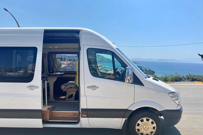 En hvid varevogn holder parkeret på en vej med udsigt over havet og bakker i baggrunden. 1