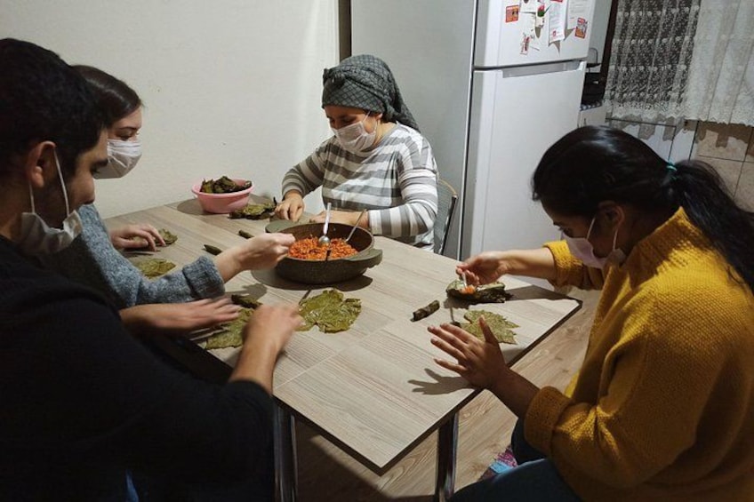 Four people preparing food at a table with bowls and leaves. 5