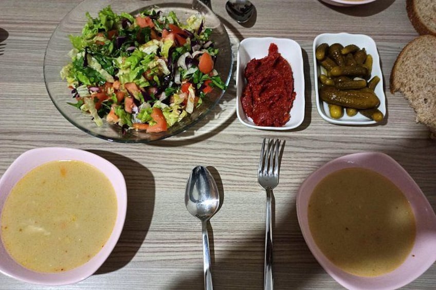 A table with various dishes including a salad, red sauce, pickles, and bowls of soup. 3