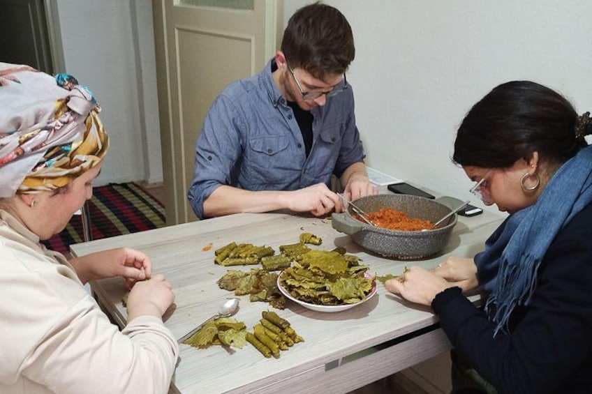 Three people preparing food at a table with a bowl of red sauce and pickled vegetables. 1