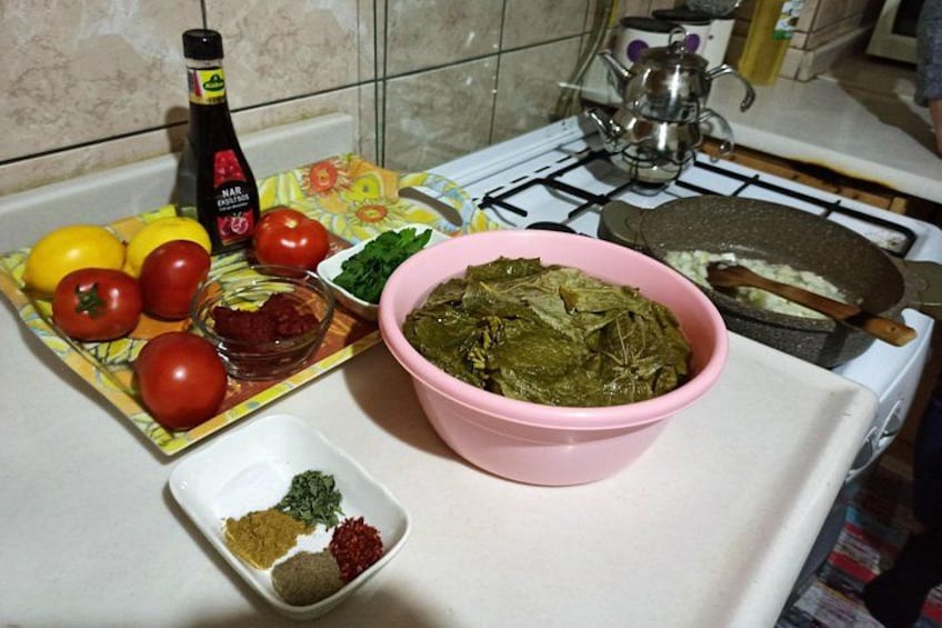 A kitchen counter with a gas stove, a pink bowl of cooked greens, a plate with tomatoes and lemons, and a bottle of cooking oil. 4