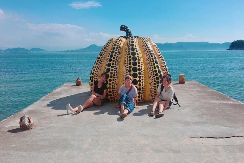 Three people sitting on a concrete pier with a large, colorful, polka-dotted sculpture in the background. 1