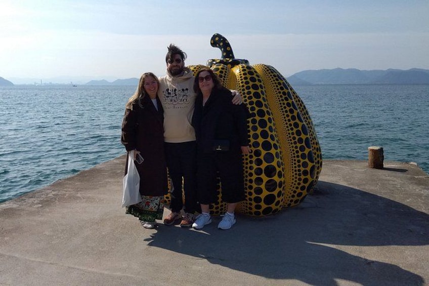 Three people standing on a concrete platform by the sea with a large yellow and black polka-dotted sculpture. 3