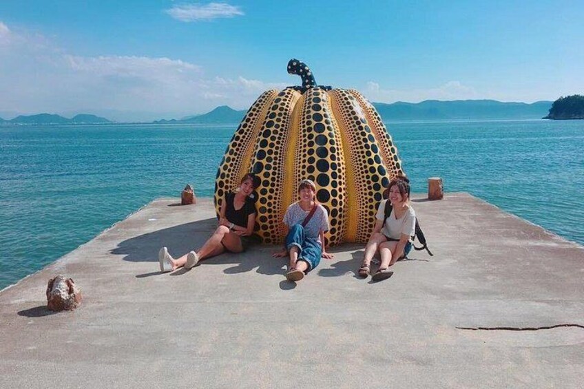 Three people sitting on a concrete pier by a large, colorful sculpture. 1