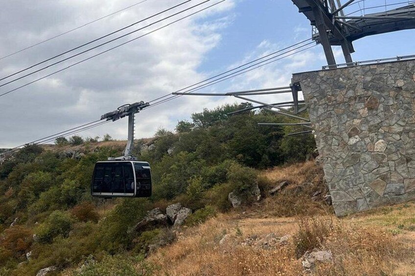 Un teleférico suspendido por cables, una pared de piedra y un paisaje montañoso con vegetación escasa. 5