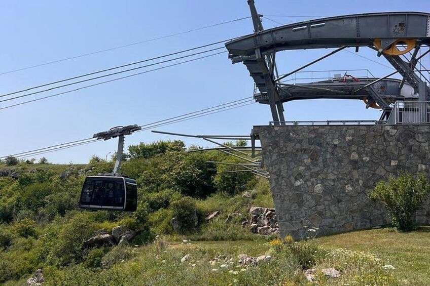 Un sistema de teleférico con un coche suspendido entre dos torres, un muro de piedra y una ladera cubierta de hierba. 4