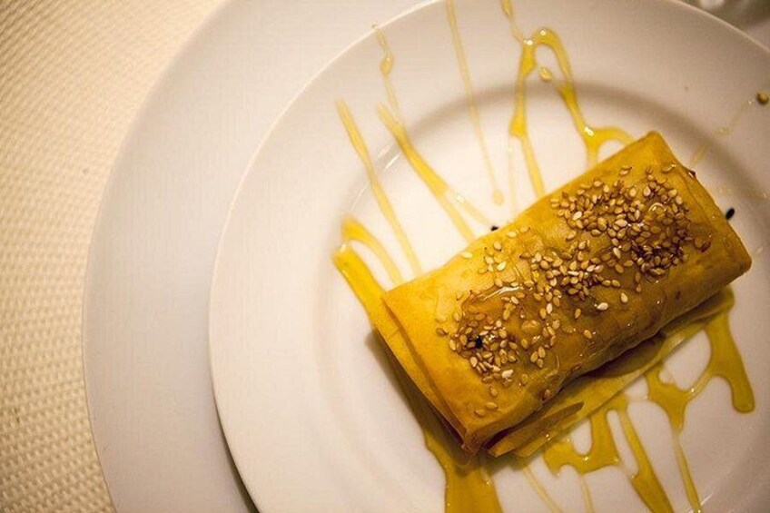 A rolled pastry with sesame seeds on a white plate with drizzled sauce. 4