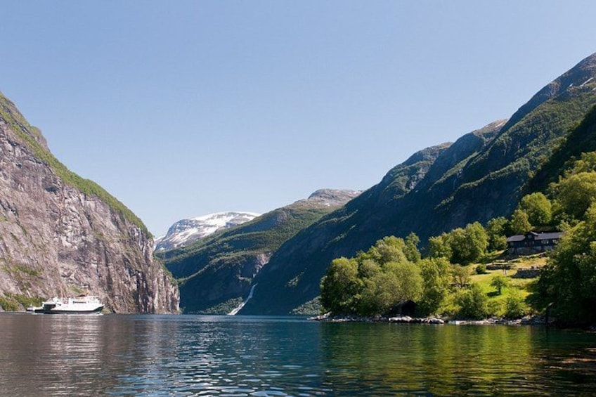 A boat on a calm lake surrounded by steep, green mountains with a clear sky. 3