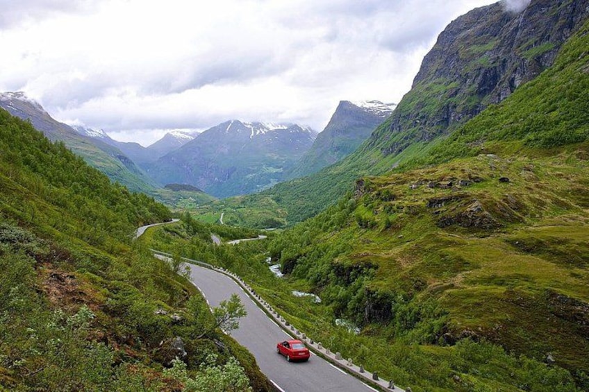 A winding road through a mountainous landscape with a red car on the road. 2
