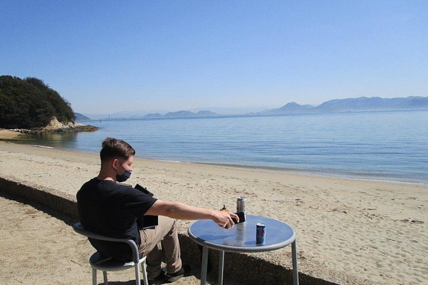 A person sitting at a table by the beach with a drink. 2