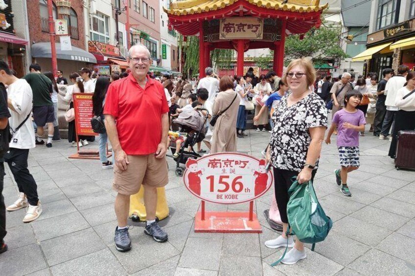 Ein Paar steht auf einem öffentlichen Platz, auf einem Schild wird das 156. Jubiläum von Kobe angegeben. 1