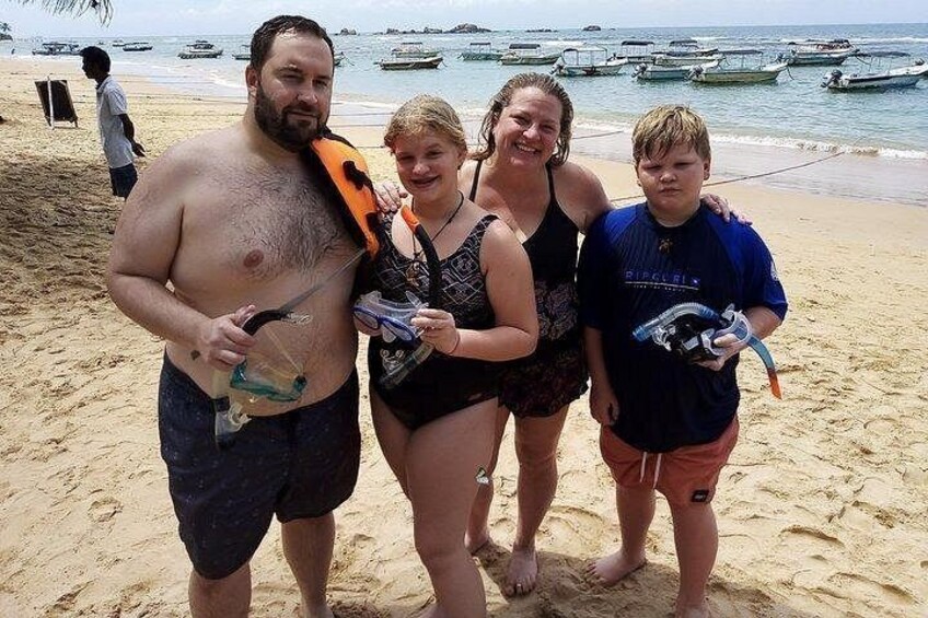 A beach with people holding fish, a sandy shore, and boats in the water. 1