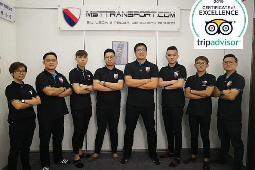 Un gruppo di persone in divisa nera che si trova in una stanza con un cartello che riporta 'MT TRANSPORT.COM' e il logo di TripAdvisor. 1