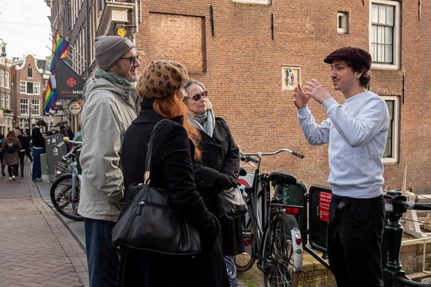 A street scene with people standing and interacting, bicycles parked along the side, and a brick building in the background. 2