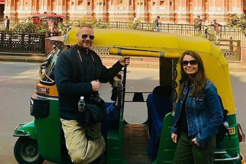 Two people standing next to a yellow and green auto-rickshaw on a street. 1